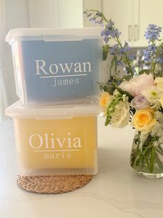 two plastic containers with flowers in them sitting on a counter next to a glass vase