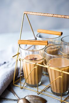 four glasses filled with liquid sitting on top of a table next to spoons and silverware