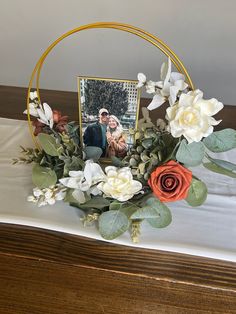 an arrangement of flowers and greenery on a table with a photo in the center