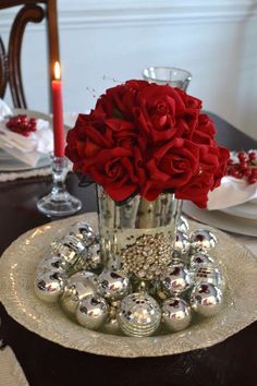 a vase filled with red roses sitting on top of a table next to silver balls