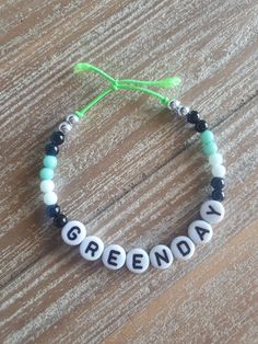 a beaded bracelet with the word green day written in white letters and beads on a wooden surface