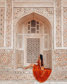 a woman in an orange dress sitting on the ledge of a white building with intricate carvings