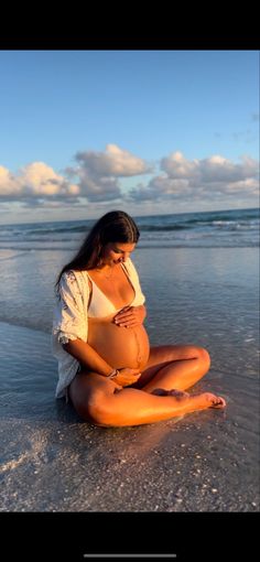 a pregnant woman is sitting on the beach