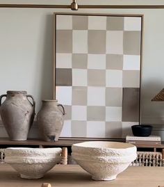 three vases and two bowls on a table in front of a framed checkered wall