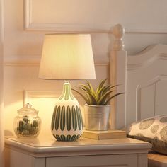 a table with a lamp, potted plant and books on it next to a bed