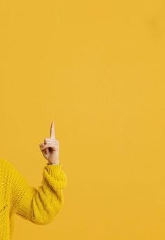 a woman in a yellow sweater points at something with her finger on a yellow background