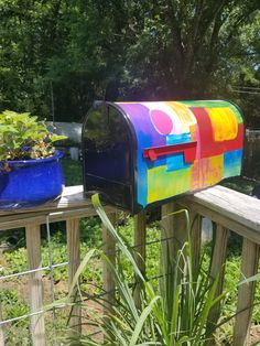 a colorful mailbox sitting on top of a wooden fence next to a potted plant