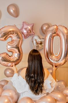 a woman in white shirt holding up balloons with the number 30 on it and surrounded by pink and gold balloons