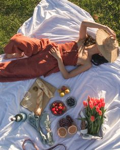 a woman laying on top of a white blanket next to flowers and fruit in bowls