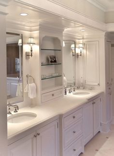 a white bathroom with double sinks and large mirrors on the wall, along with built - in shelving