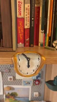 there is a clock that is on the shelf in front of some books and other items