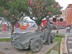 a statue of a man sitting on top of a car next to a tree with pink flowers