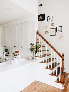 a white kitchen with wooden floors and stairs leading up to the upper floor, along with pictures on the wall