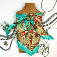 Patterned scarf in Taos Valley. Scarf is tied around a wooden piece. The scarf and piece of wood is pictured on a white background with Navajo jewelry spread out around it. Cowboy Copper, Giddy Up Glamour, Online Closet, Taos, New Line, Tao, Cowboy