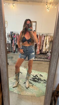 a woman taking a selfie in front of a mirror with her cowboy boots on