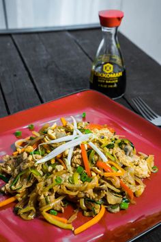 a red plate topped with noodles and vegetables next to a bottle of alcohol on a wooden table