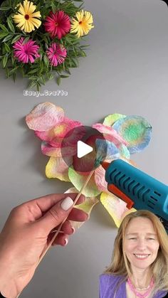 a woman is making a flower out of tissue paper with a blow dryer on her head