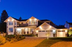 a large house with lights on in the front yard and driveway at night, lit up by outdoor lighting