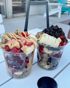 two plastic cups filled with different types of desserts on top of a white table