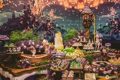 a table filled with cakes and cupcakes next to a wall covered in lights