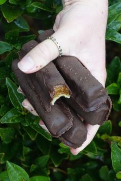 a person holding two pieces of chocolate in their hand with green leaves around them and one half eaten