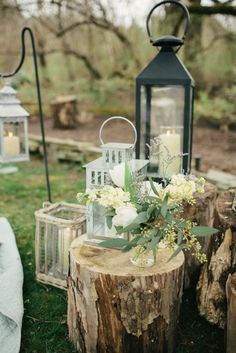 an outdoor wedding setup with lanterns, flowers and candles on the side of a tree stump