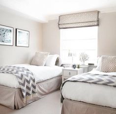 two beds in a bedroom with white walls and carpeted flooring next to windows