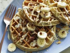 a blue plate topped with waffles covered in banana slices and nuts next to a fork