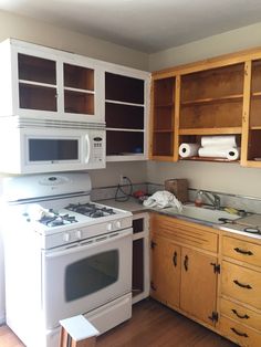 an empty kitchen with white appliances and wooden cupboards on either side of the stove