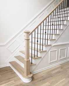 a white staircase with black railing and wooden handrails in an empty room next to a wood floor