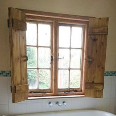 a bath tub sitting under a window next to a tiled floor and wall with wooden shutters