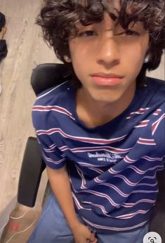 a young man with curly hair sitting in a chair