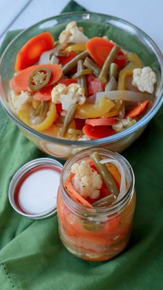 a glass bowl filled with vegetables next to a jar of ranch dressing on top of a green cloth