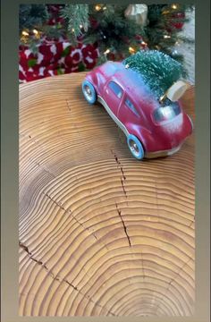 a red toy car with a christmas tree on it's roof sitting on top of a log