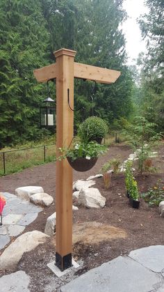 a bird feeder in the middle of a garden with rocks and trees around it,