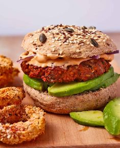 a sandwich with meat and vegetables on a wooden cutting board next to some onion rings