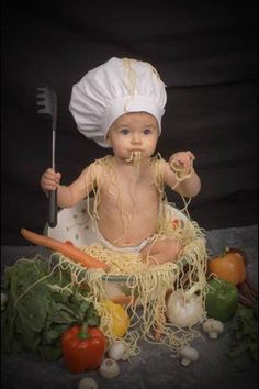 a baby sitting on top of a pile of vegetables wearing a chef's hat