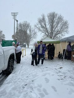 several people standing in the snow near a tent and cars parked on the side of the road