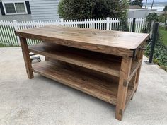 a wooden table sitting on top of a cement ground next to a white picket fence