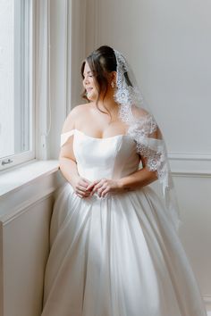 a woman in a wedding dress standing next to a window with her hands on her hips