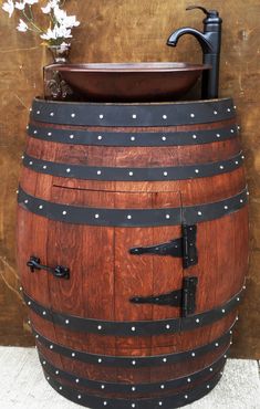 a large wooden barrel with metal straps and rivets on the bottom, in front of a brown wall