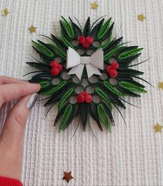 someone is making a paper christmas wreath with red berries and green leaves on it's side