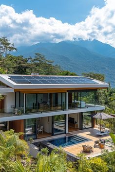 a house with a solar panel on the roof is surrounded by greenery and mountains