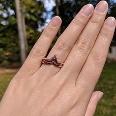 a woman's hand with a diamond ring on top of her finger and trees in the background