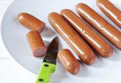 several hot dogs on a white plate with a green knife and fork next to them