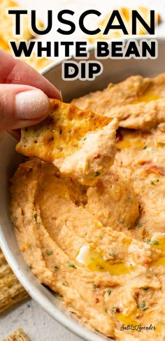 a hand dipping a tortilla chip into a white bean dip in a bowl