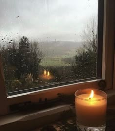 a candle sitting in front of a window on a rainy day