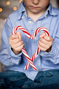 a young boy holding two candy canes in front of his heart - shaped frame