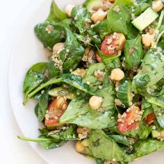 a white plate topped with spinach salad and chickpeas covered in sesame seeds