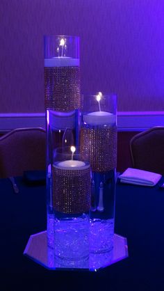 three lit candles sitting on top of a table in front of a purple wall and chairs